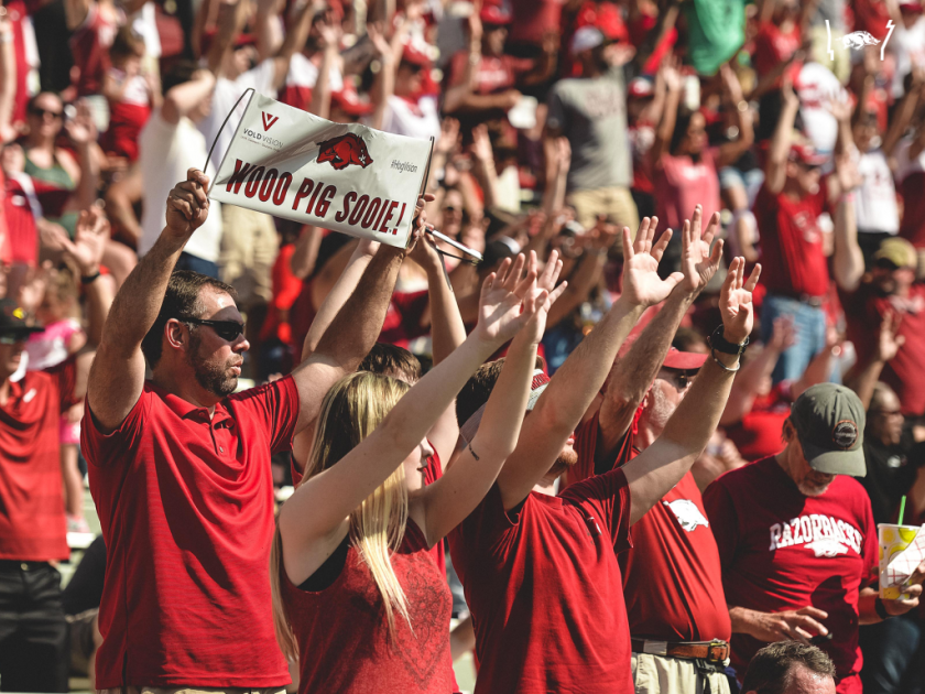 Arkansas Razorbacks fans in red raising their arms during the Woo Pig Sooie Hog Call